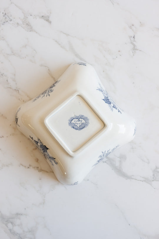 A white, square floral bowl made of porcelain features delicate blue flower patterns and slightly flared edges, resting upside down on a white marble surface—perfectly sized for elegant table settings.