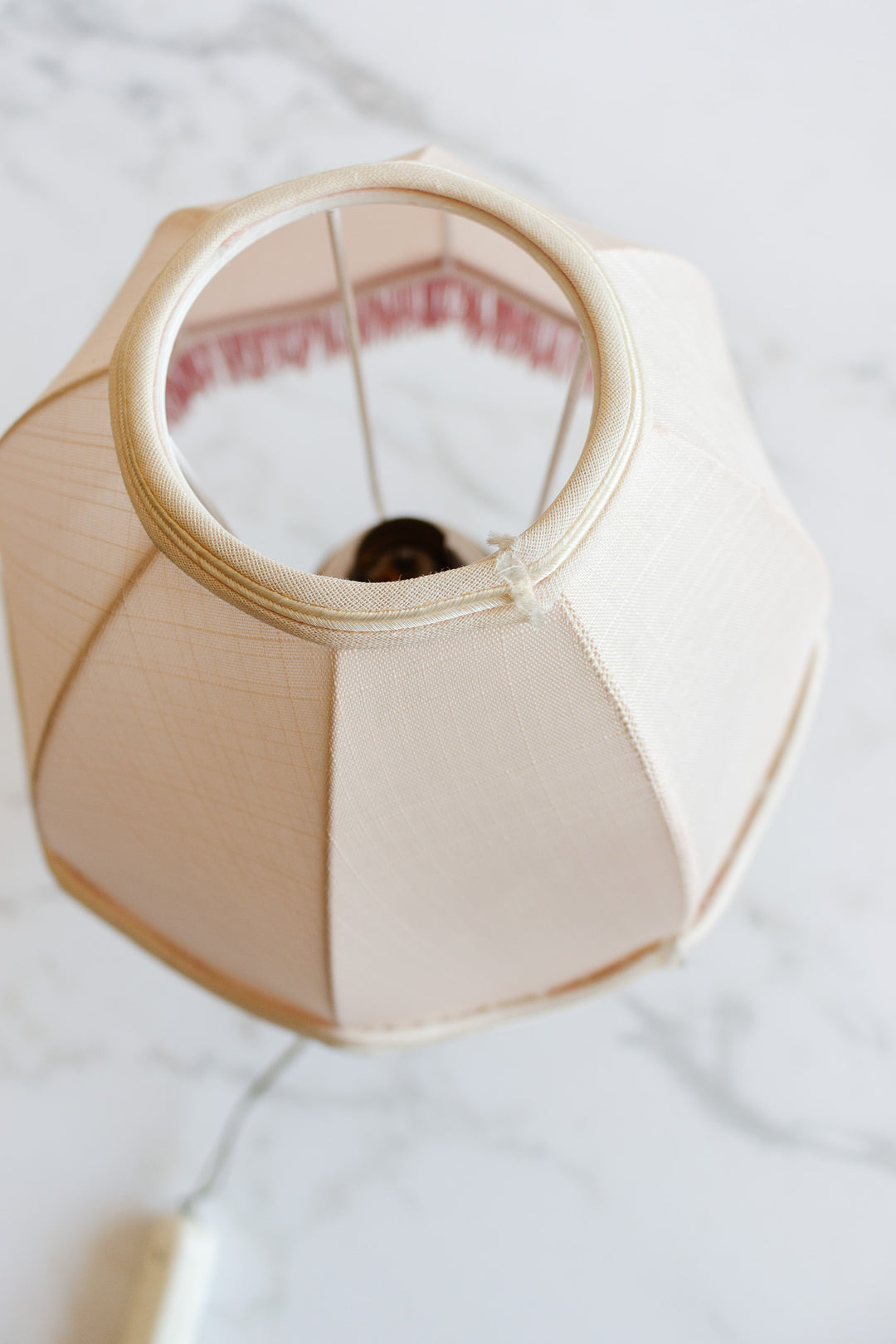 A top-down view of the lamp's beige lampshade displays its dimensions, bulb socket, and harp on a white marble surface.