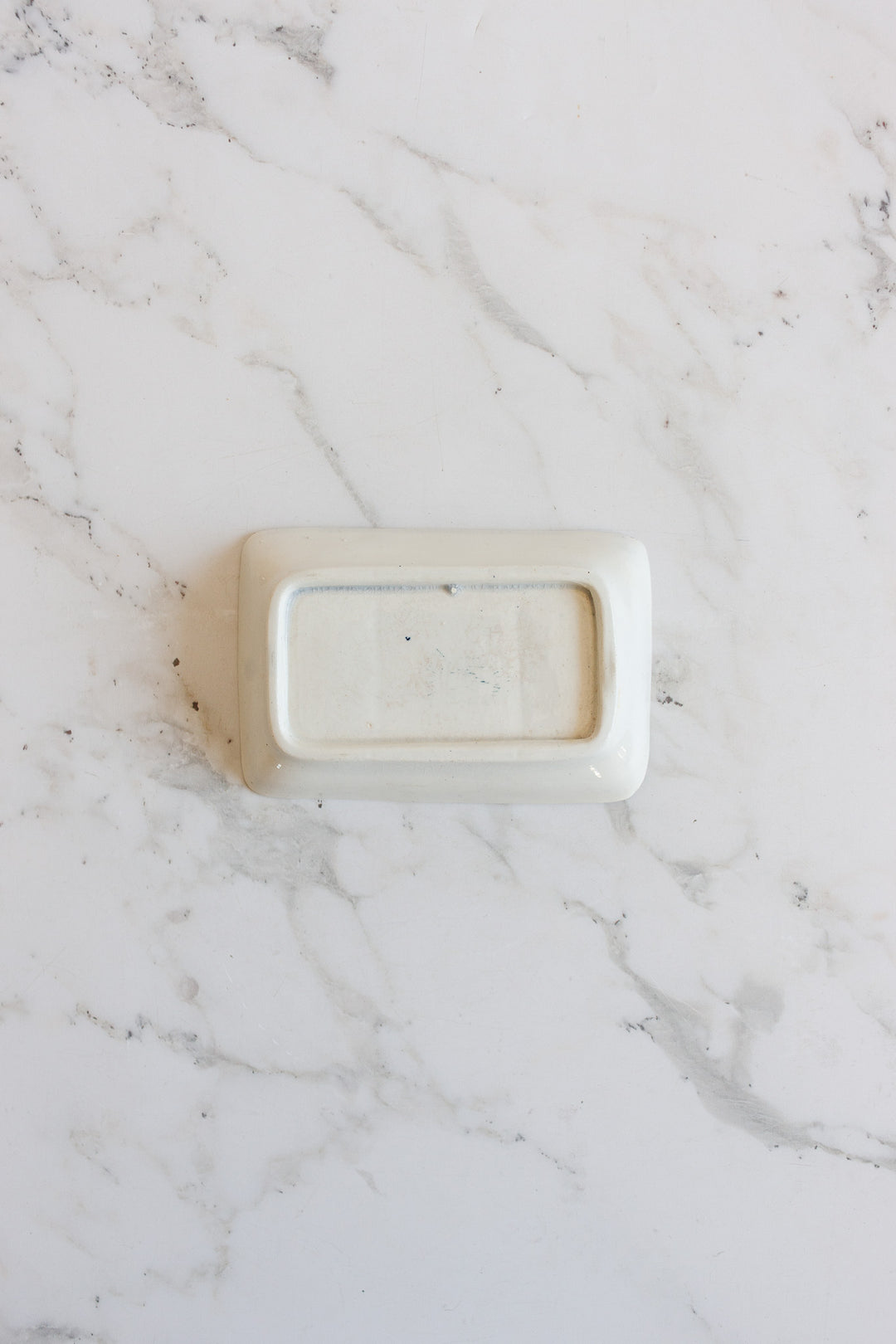 A compact, rectangular white soap holder sits upside down on a white marble surface with subtle grey veining.