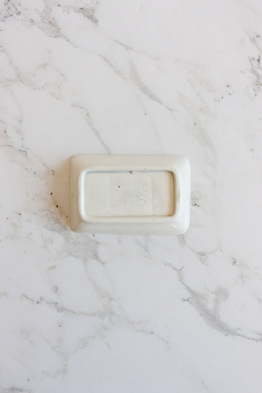 A compact, rectangular white soap holder sits upside down on a white marble surface with subtle grey veining.