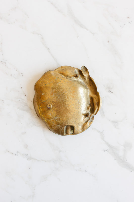 A brass trinket dish with a raised rabbit design and irregular dimensions rests on a white marble surface.