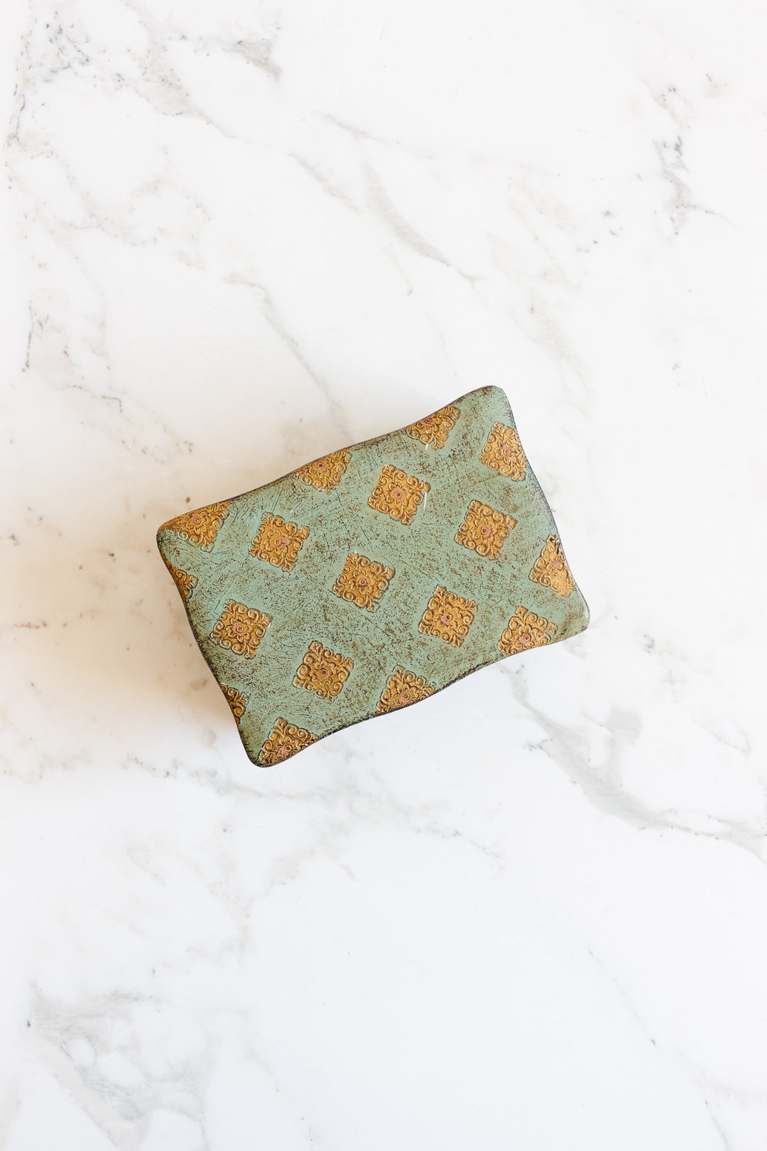 The florentine box features a greenish fabric with a repeating gold ornate square pattern and precise rectangular dimensions, elegantly displayed on a white marble surface.
