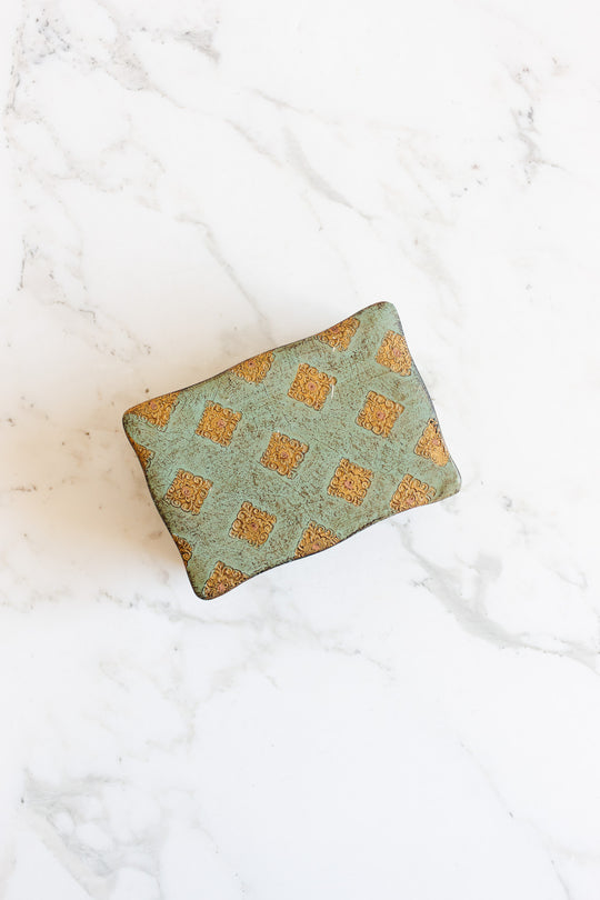 The florentine box features a greenish fabric with a repeating gold ornate square pattern and precise rectangular dimensions, elegantly displayed on a white marble surface.