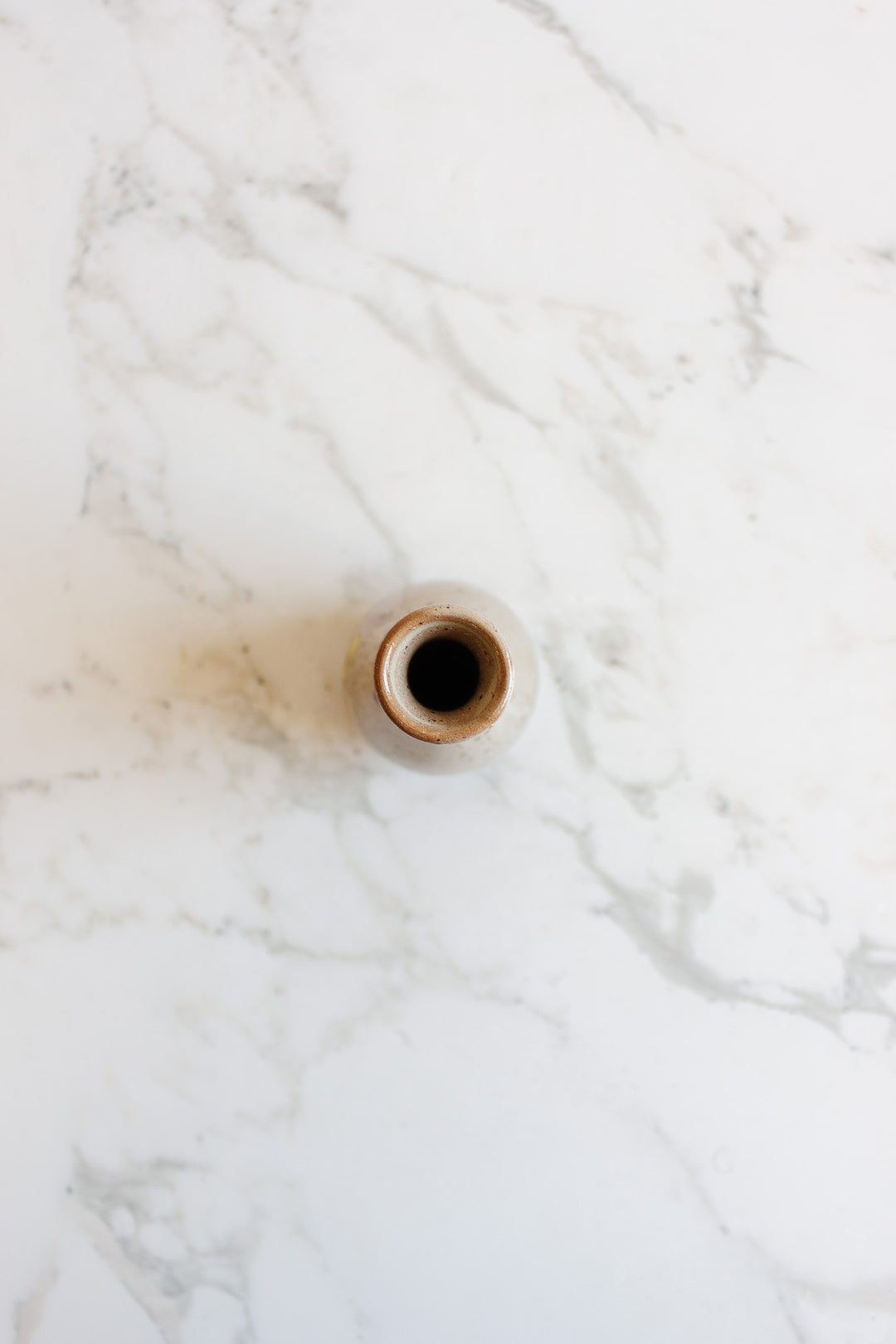 The speckled vase, a small round ceramic piece with a narrow opening, is captured from above, showcasing its elegant form as it sits on white marble with grey veining.