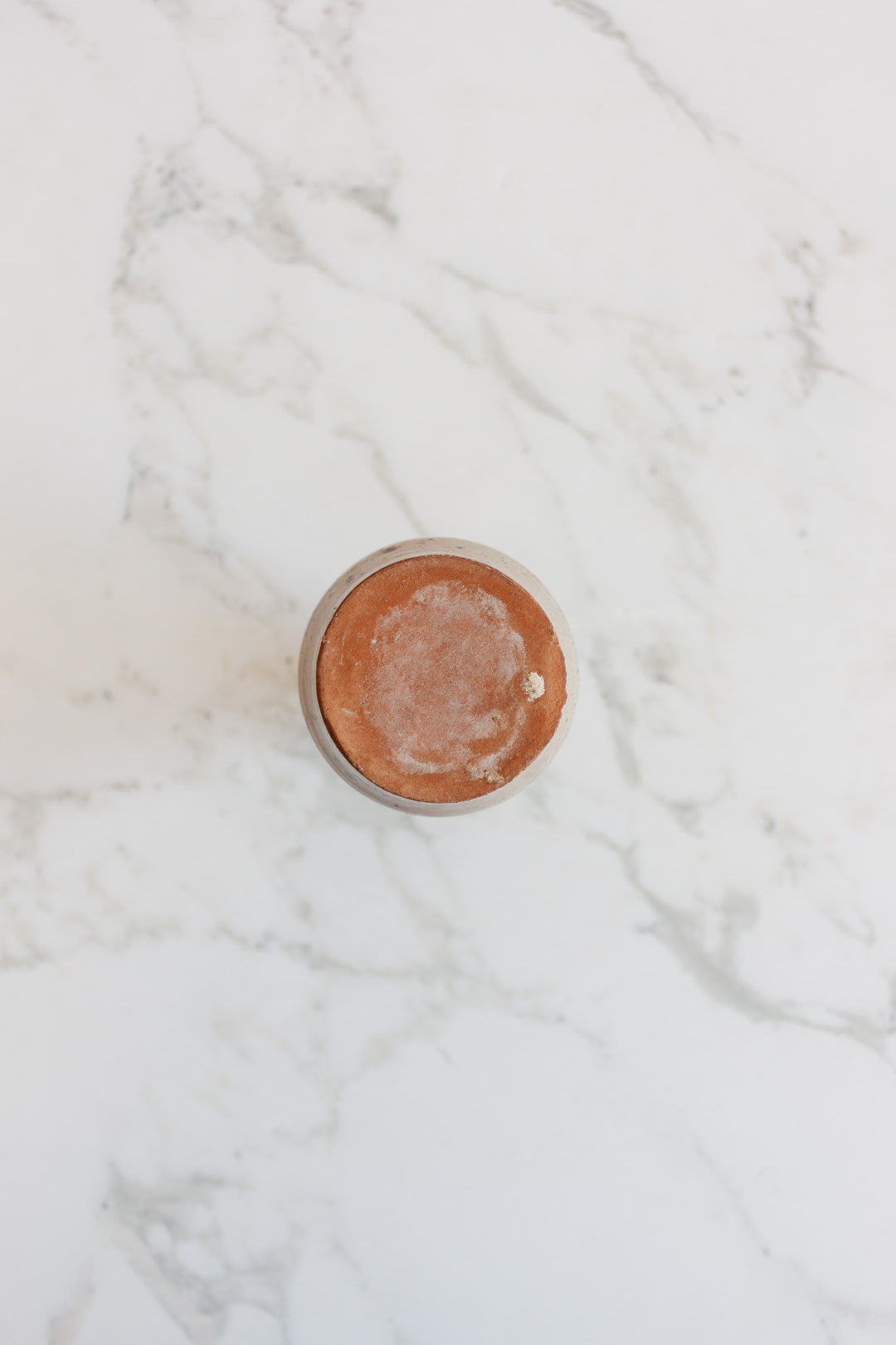 A speckled vase with a compact, round design is seen from above, resting on white marble with gray veining, showcasing its simple elegance.