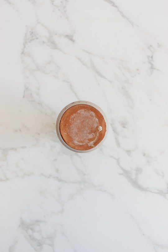 A speckled vase with a compact, round design is seen from above, resting on white marble with gray veining, showcasing its simple elegance.