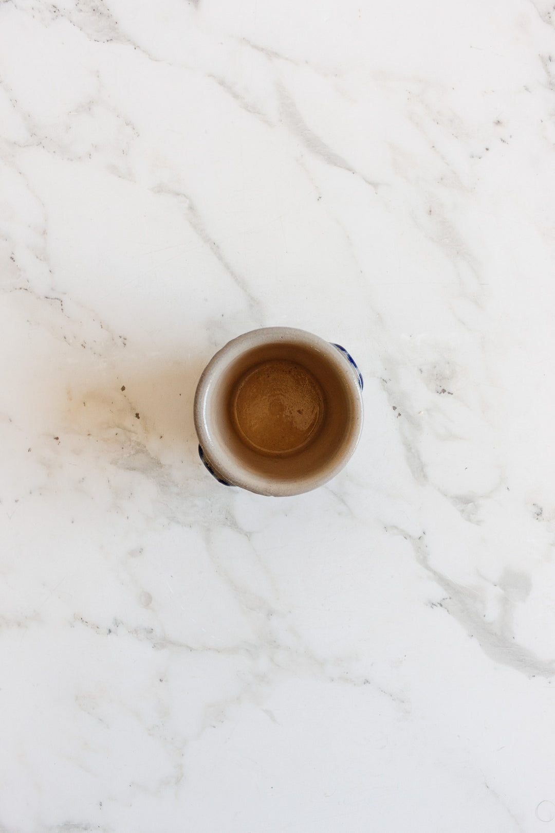 A minimalist salt cellar, compact and empty, is viewed from above on a white marble surface with light gray veining.