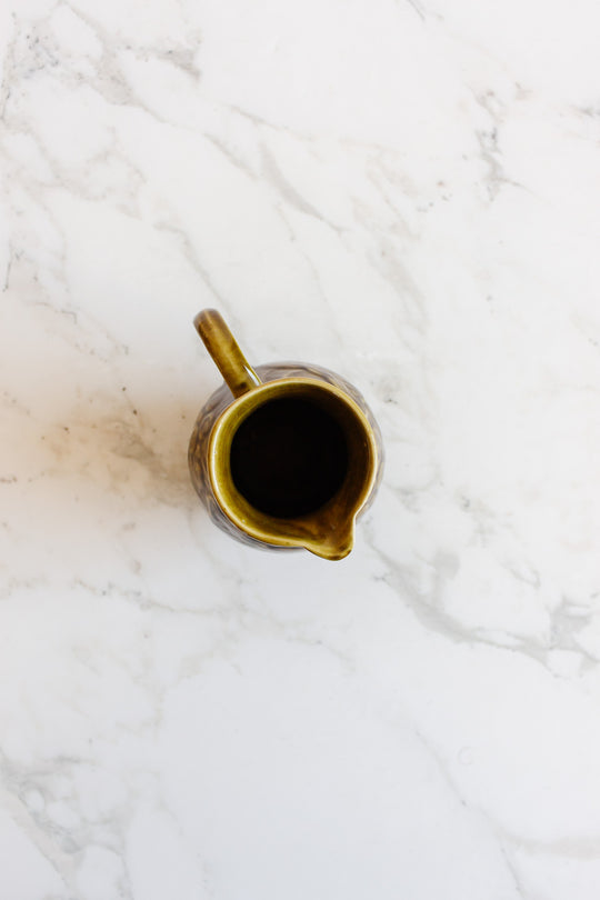 A compact brown ceramic pitcher with a handle from the drinkware set rests on a white marble surface, viewed from above—perfect for serving.