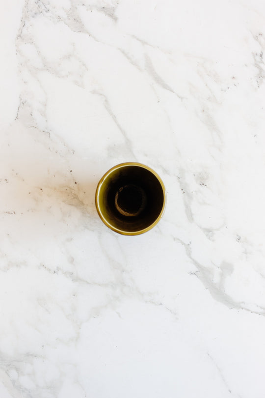 A drinkware set featuring compact, dark-toned espresso cups is displayed on a white marble surface with gray veining, emphasizing their elegant, minimalist design.