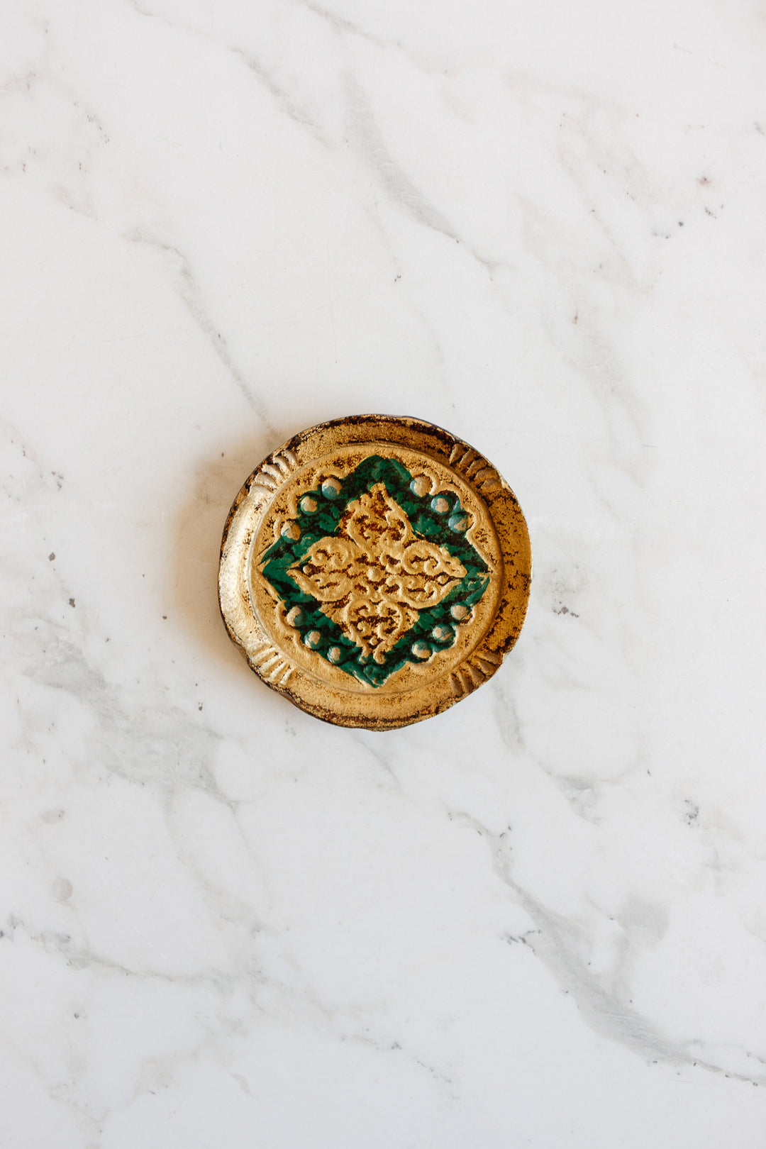 A set of small, round ceramic florentine coasters with a green and yellow geometric pattern, ideal for snacks or drinks, displayed on a white marble surface.