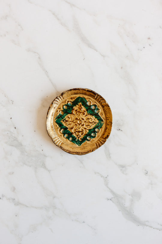 A set of small, round ceramic florentine coasters with a green and yellow geometric pattern, ideal for snacks or drinks, displayed on a white marble surface.