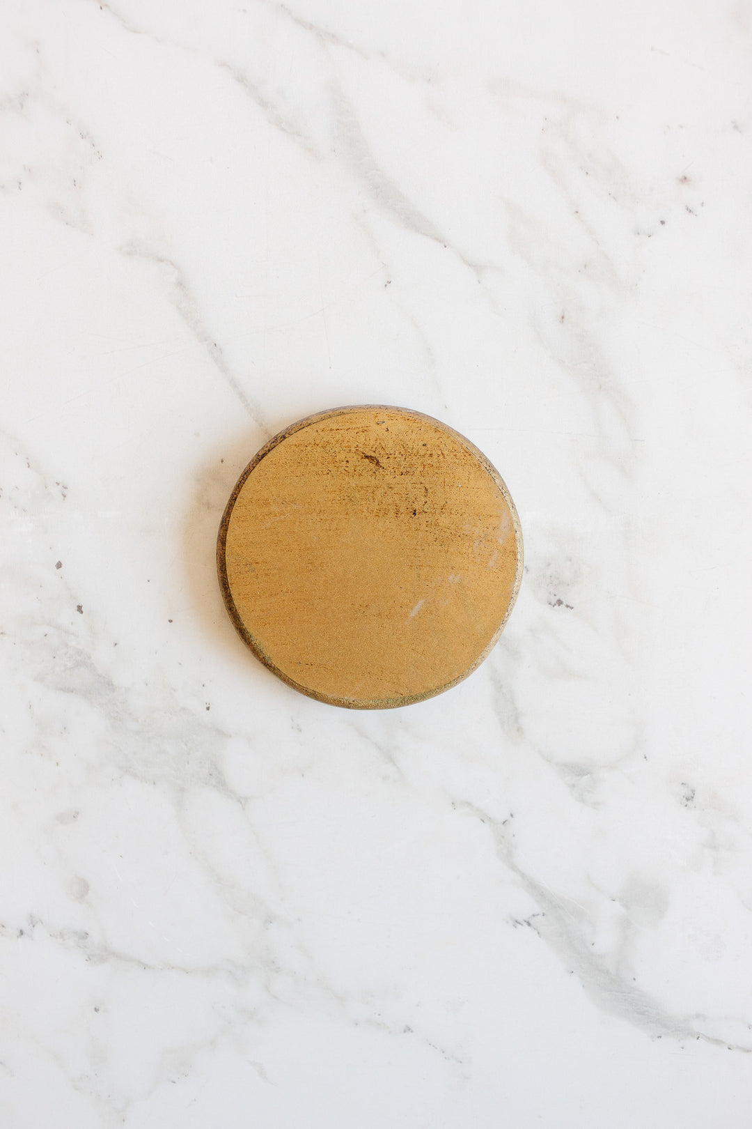 A set of round gold Florentine coasters with sleek dimensions rests elegantly on a marble surface.
