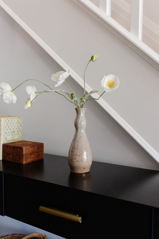 A speckled vase with white flowers is displayed on a black table beside a wooden box and a book, set before a light stairway with white railings—ideal for showcasing décor of any size.