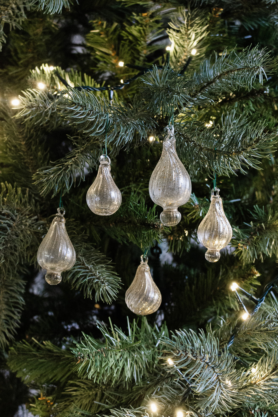 An antique Italian hand blown glass ornament with aventurine gold inclusions hangs on a Christmas tree, surrounded by green needles and warm white string lights.