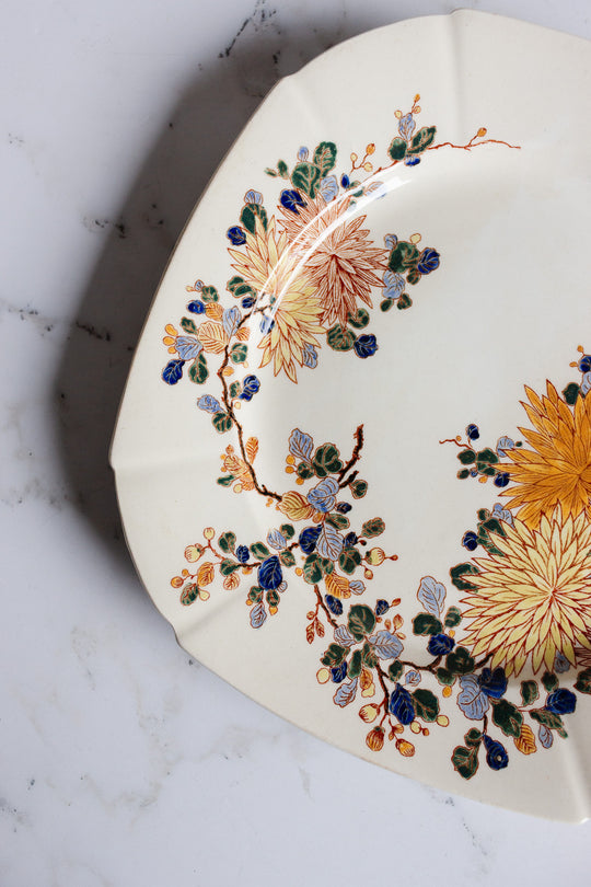 A partial view of a turn of the century Gien transferware cake plate, cream-colored with scalloped edges and floral design, sits on white marble—ideal for adding French charm to any table.