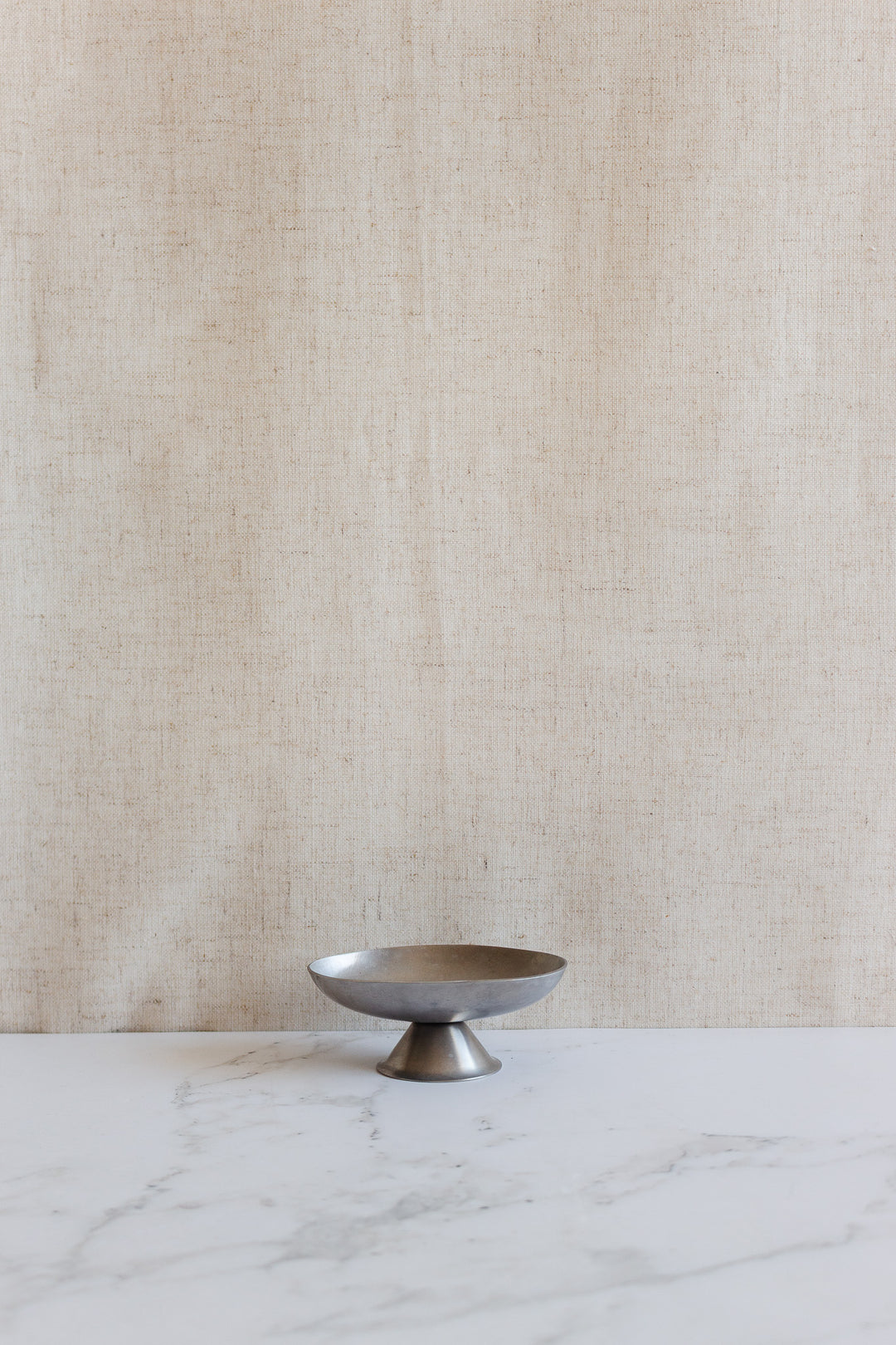 A vintage French stainless steel oblong ice cream cup rests empty on a white marble surface with a beige textured fabric backdrop.