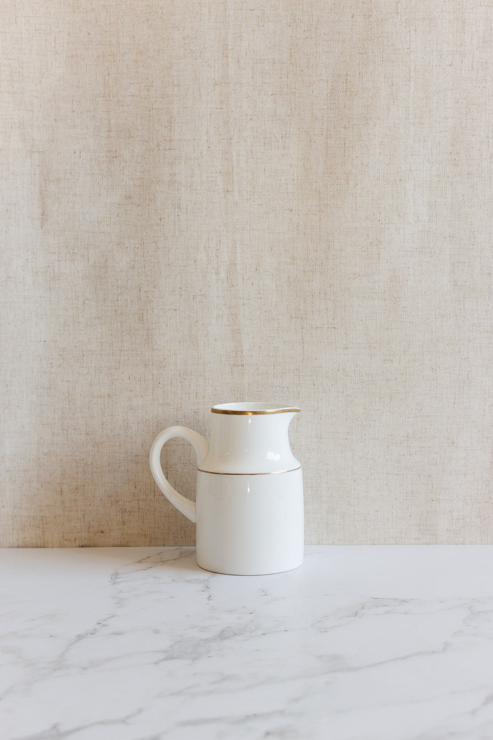 A vintage Wedgwood “Metallised” bone china milk jug with a handle sits on a marble surface against a beige textured background.