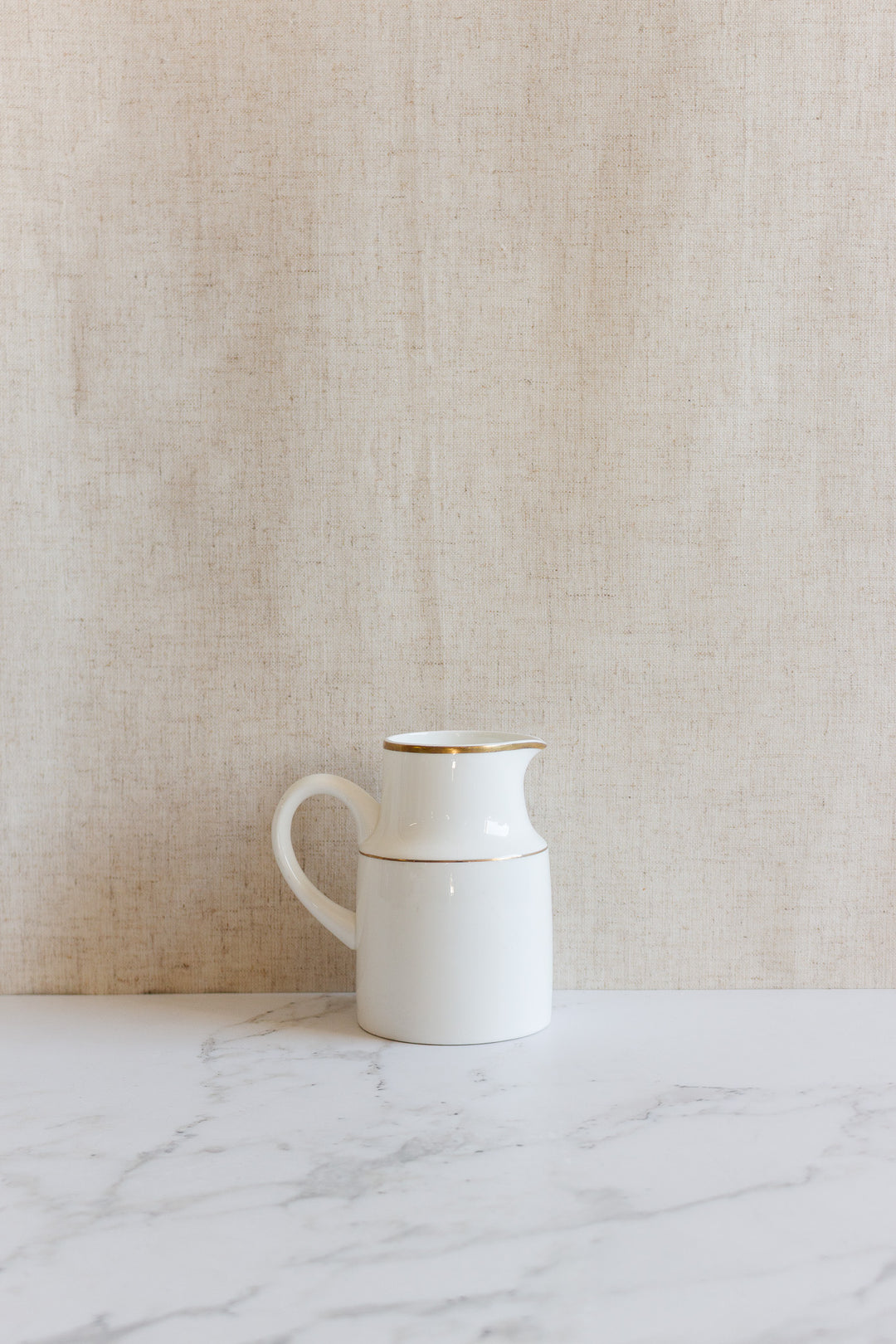 A vintage Wedgwood “Metallised” bone china milk jug with a handle sits on a marble surface against a beige textured background.