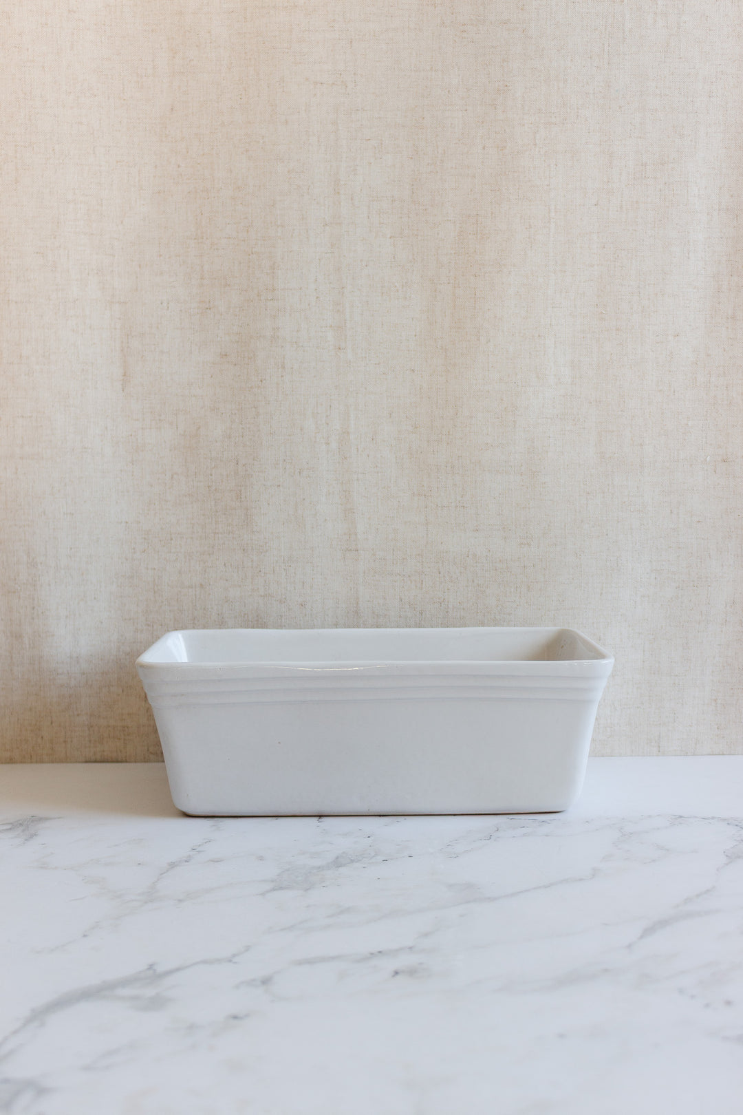 A vintage French glazed terracotta cotta terrine sits on a marble countertop in front of a light beige textured background.