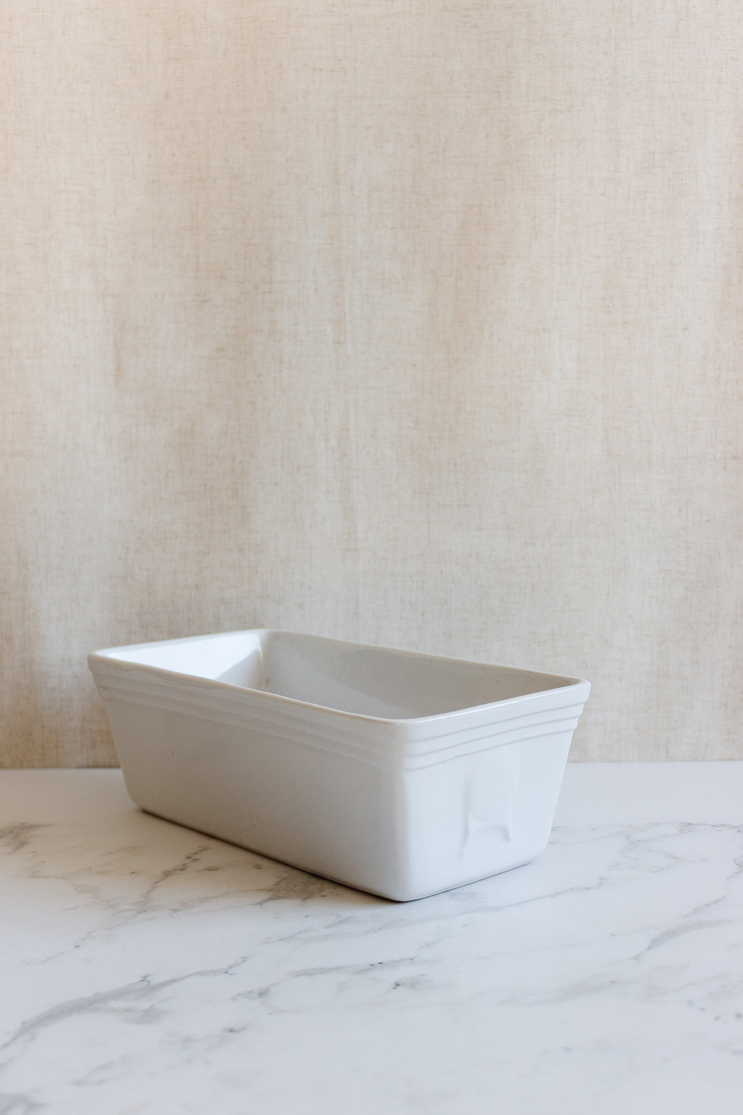 A vintage French glazed terracotta cotta terrine sits on a marble surface against a light beige textured background.