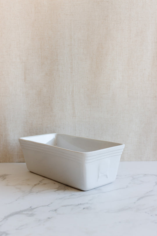 A vintage French glazed terracotta cotta terrine sits on a marble surface against a light beige textured background.