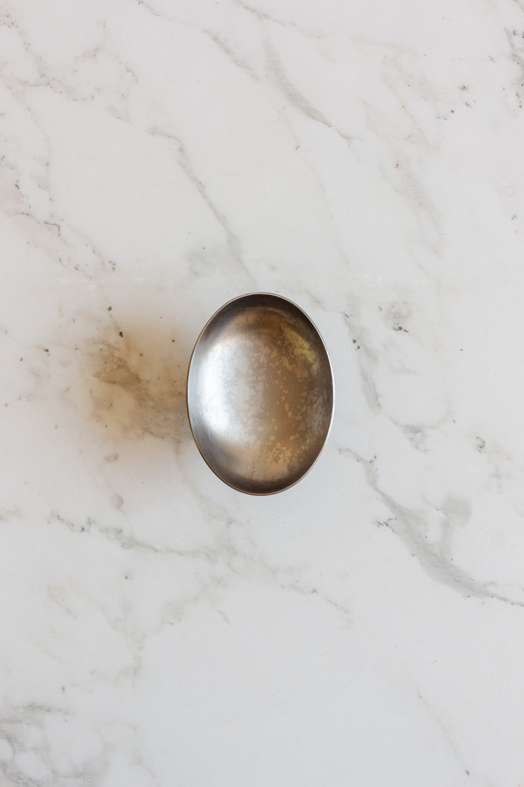A vintage French stainless steel oblong ice cream cup sits empty on a white marble surface with light grey veining, evoking classic brasserie tableware.