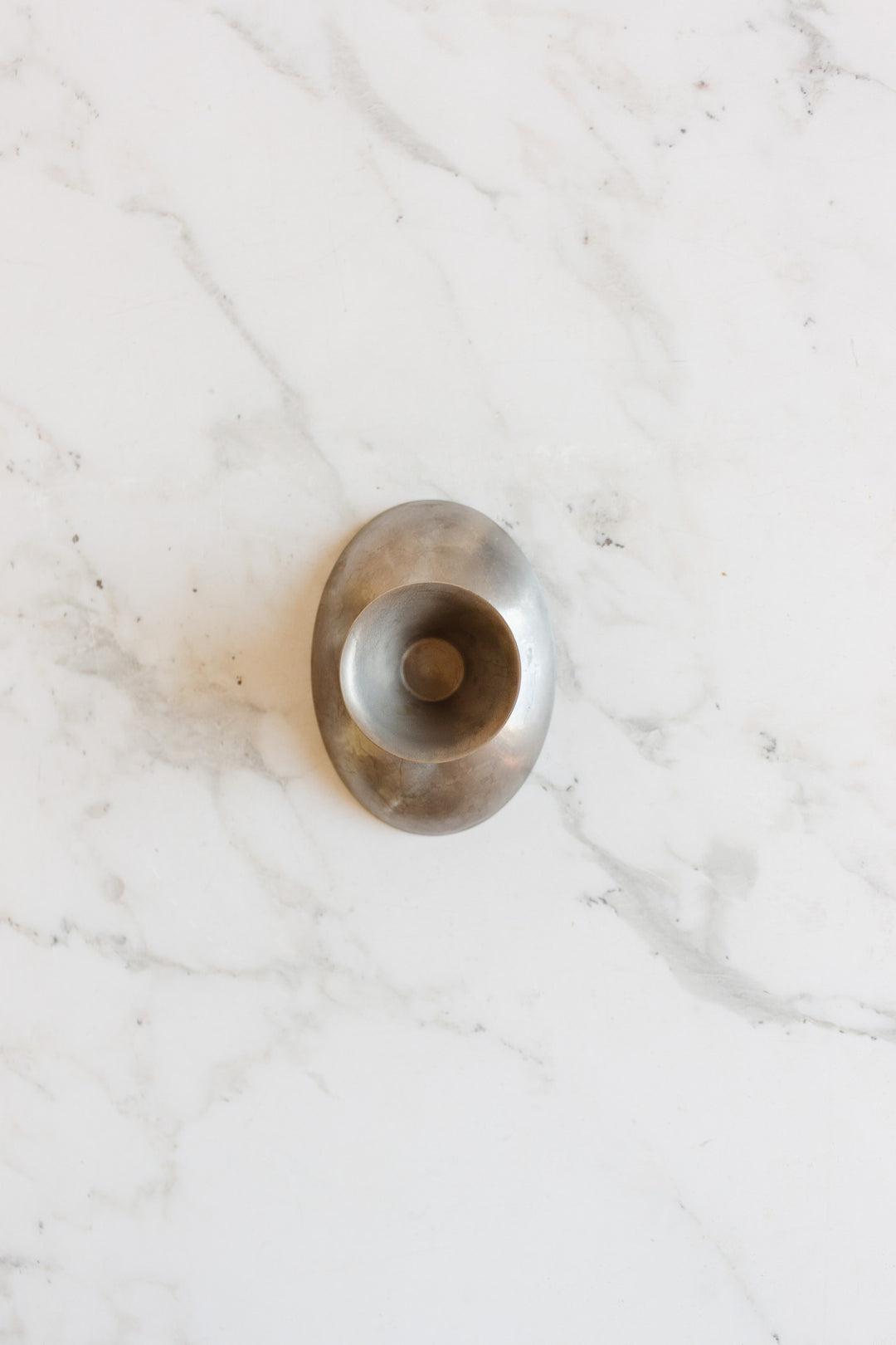 A vintage French stainless steel oblong ice cream cup, with smooth lines evoking a mid-century aesthetic, rests on a white marble surface veined in grey.