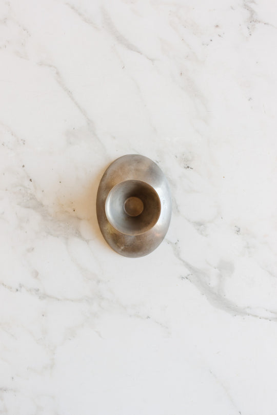 A vintage French stainless steel oblong ice cream cup, with smooth lines evoking a mid-century aesthetic, rests on a white marble surface veined in grey.
