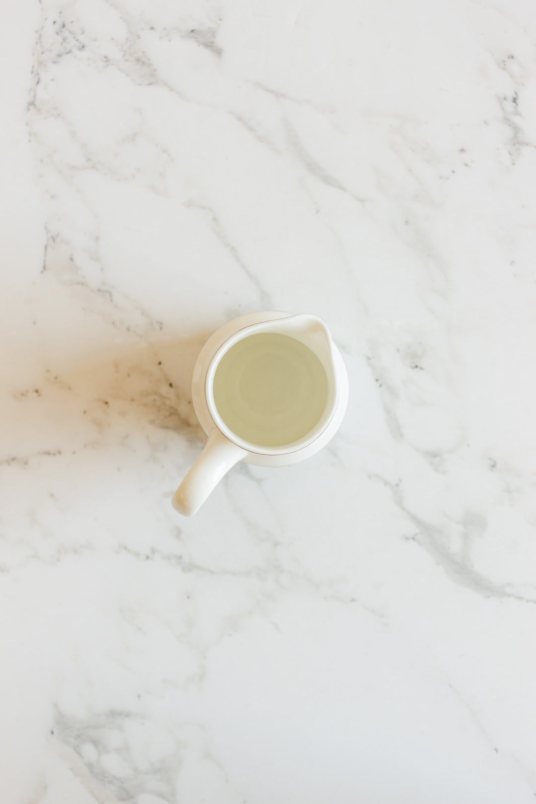 A vintage Wedgwood "Metallised" bone china milk jug filled with water sits on a white marble surface, viewed from above.