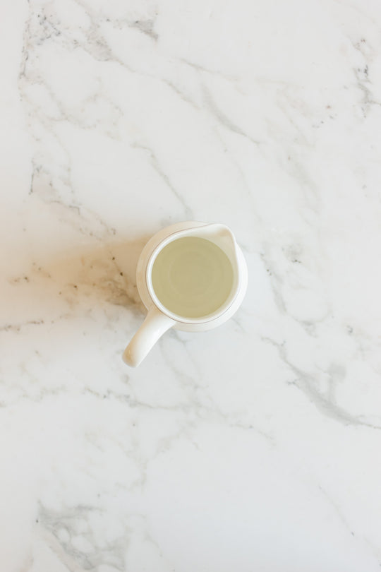 A vintage Wedgwood "Metallised" bone china milk jug filled with water sits on a white marble surface, viewed from above.