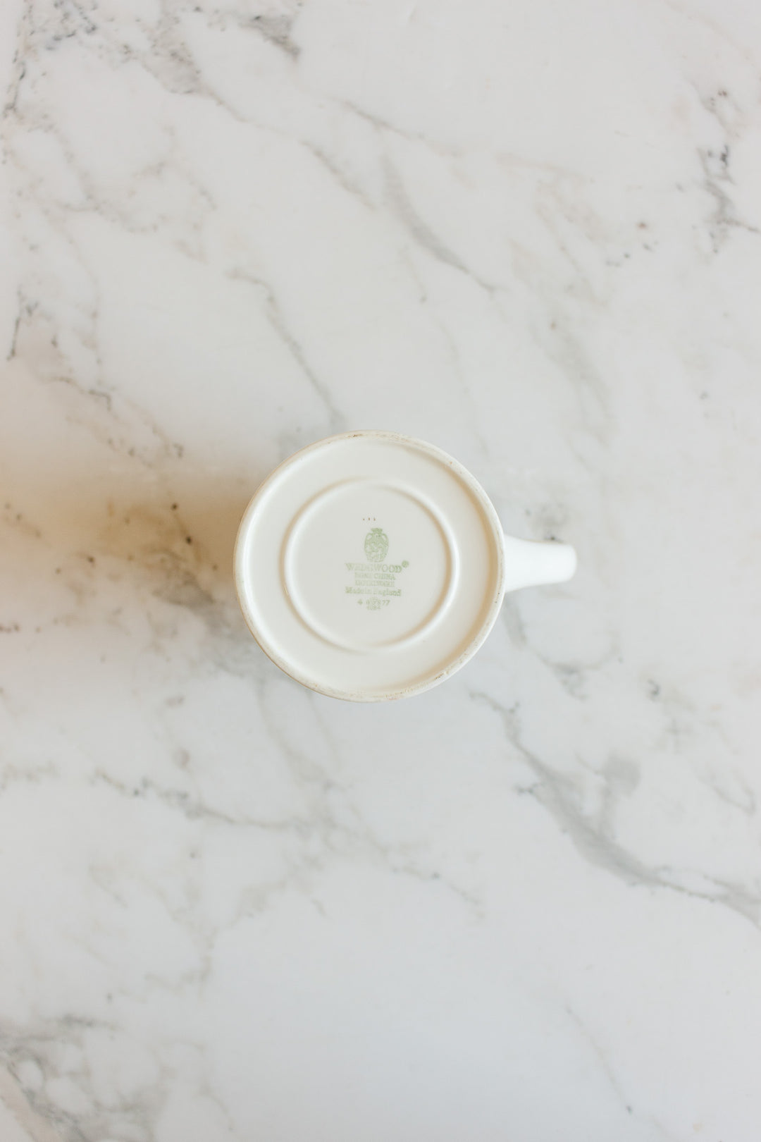 A vintage Wedgwood “Metallised” bone china milk jug sits upside down on a white marble surface, revealing the mark and logo on its base.
