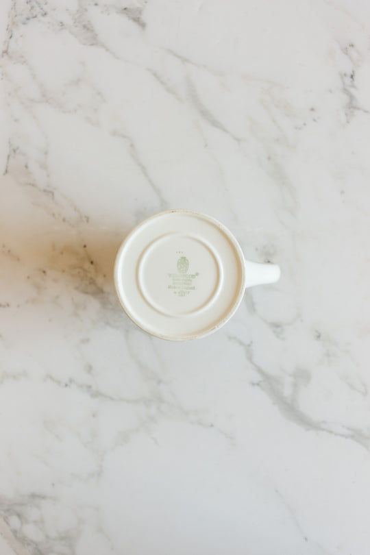 A vintage Wedgwood “Metallised” bone china milk jug sits upside down on a white marble surface, revealing the mark and logo on its base.