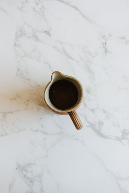 A vintage French "grès de berry" stoneware pitcher with a handle, inspired by traditional French pottery, is viewed from above as it rests on a white marble surface with subtle gray veining.
