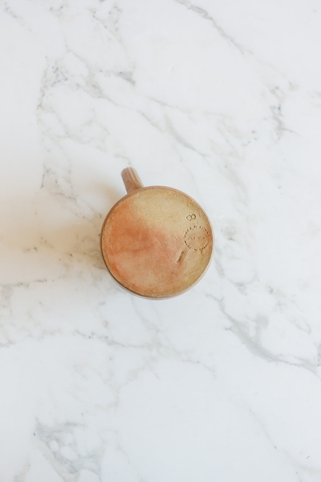 A vintage French "grès de berry" stoneware pitcher sits upside down on a white marble surface, showcasing its circular base, handle, and the stamped Grès de Berry mark.