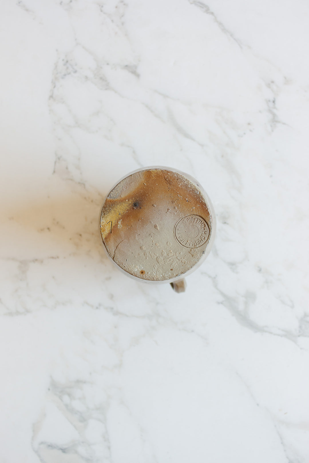 A top view of iced coffee with swirled cream on white marble sits beside a midcentury french stoneware vessel by H. Chevalier & fils, orléans, evoking pottery charm and a marbled effect.