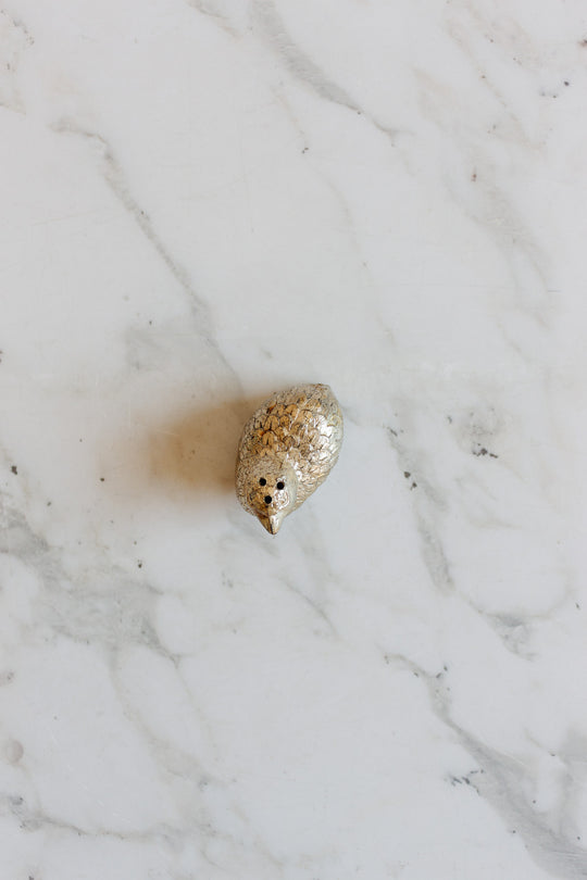 A pair of 1970s Italian silver plate quail salt and pepper shakers with textured feathers sits on white marble, evoking vintage table decor.