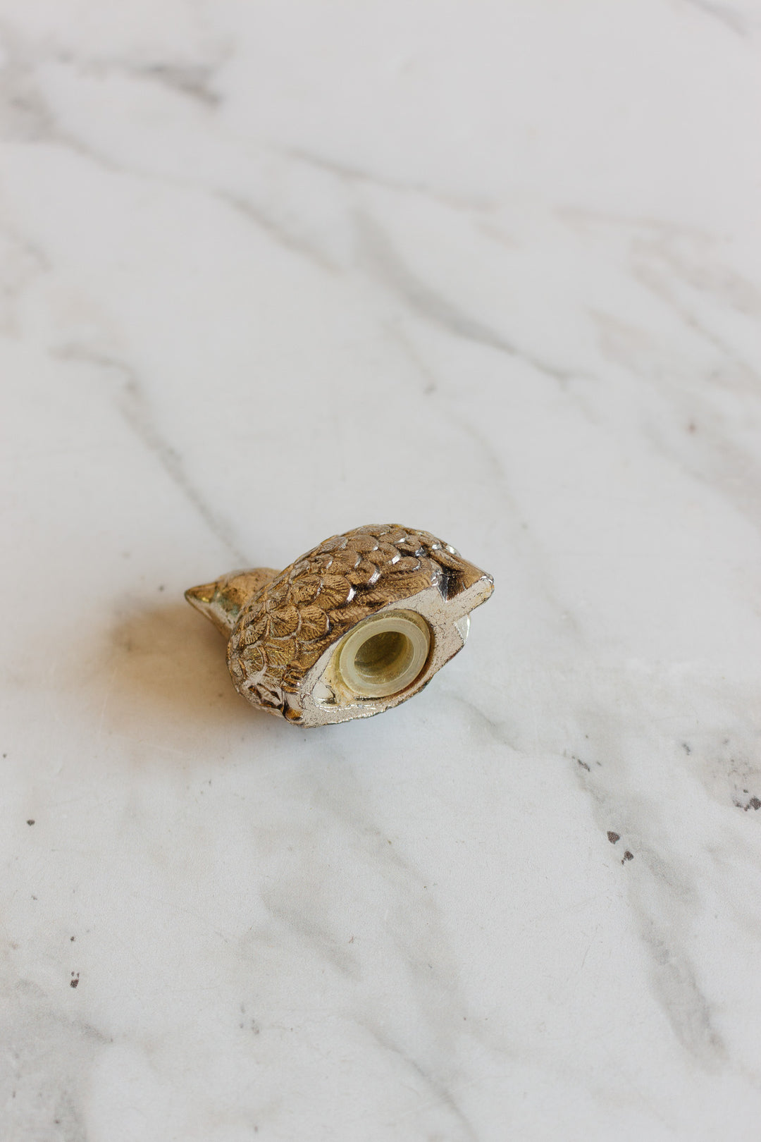 A 1970s Italian silver plate quail salt and pepper shaker rests on its side atop a white marble surface, with the shaker’s bottom opening visible—evoking classic vintage table decor.
