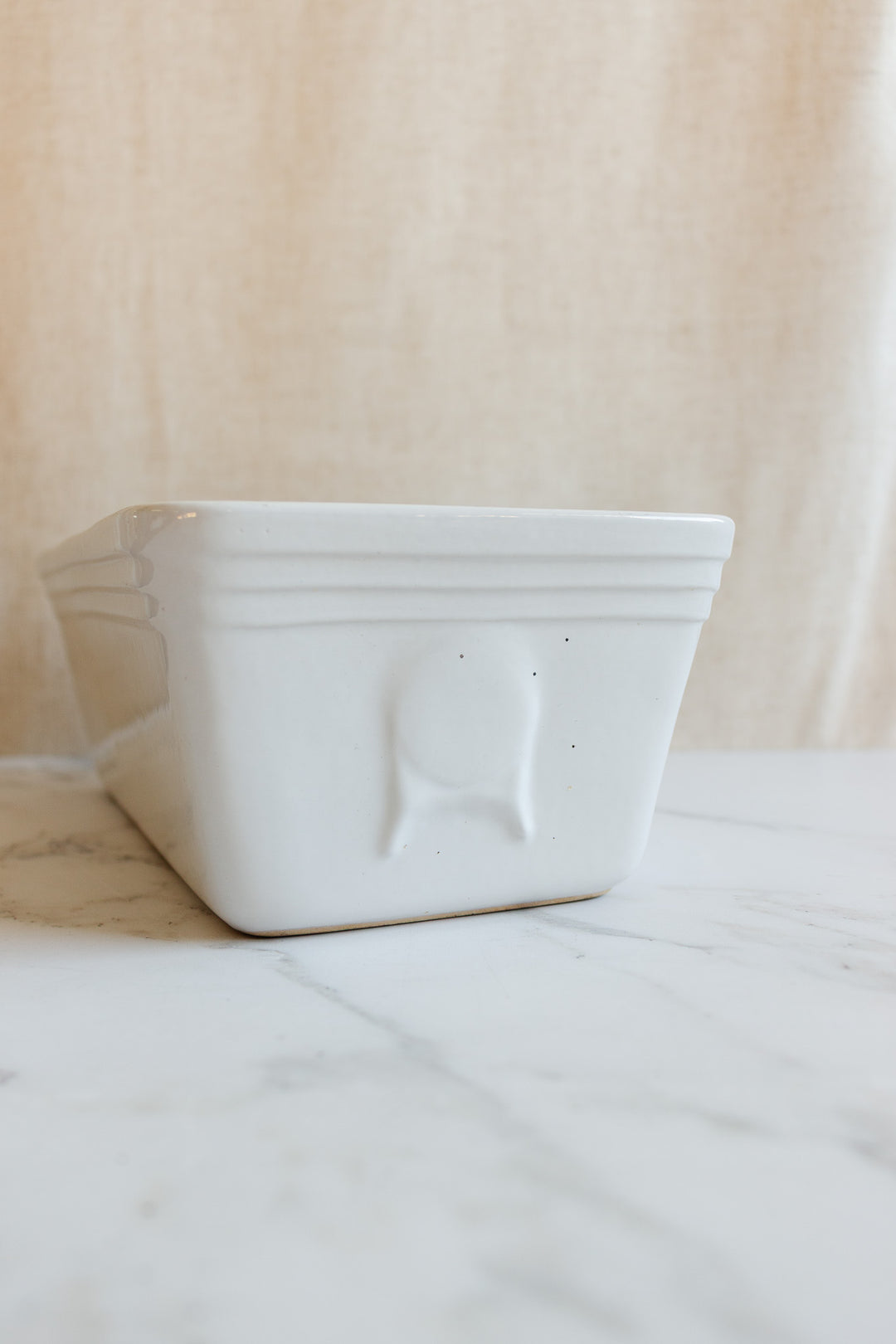 A vintage French glazed terracotta terrine sits on a marbled surface with a textured beige background. Subtle embossed lines near the rim and a small round design offer an elegant farmhouse touch to this classic kitchenware.