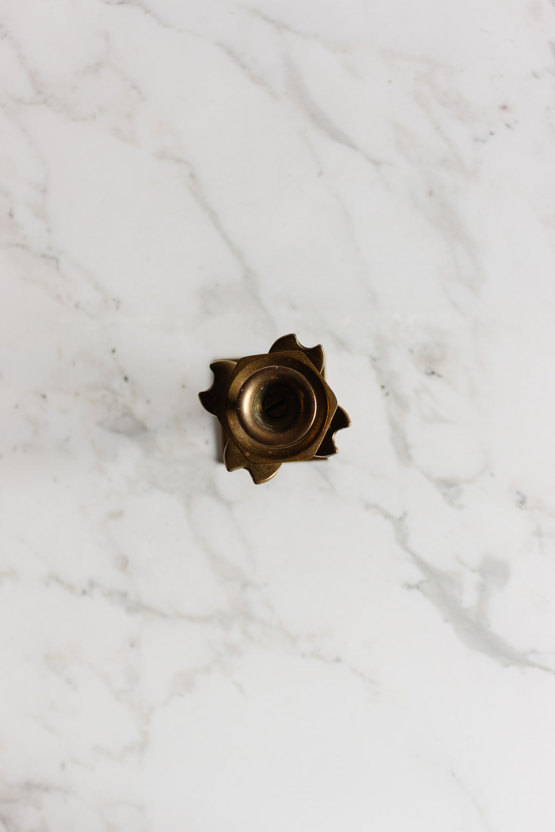 A pair of metallic candleholders with precise shapes and central holes is placed on a white marble surface.