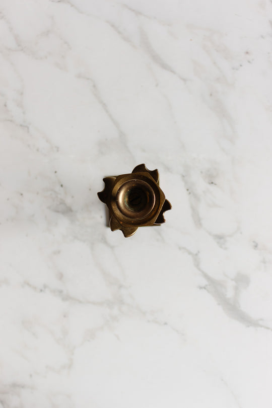 A pair of metallic candleholders with precise shapes and central holes is placed on a white marble surface.