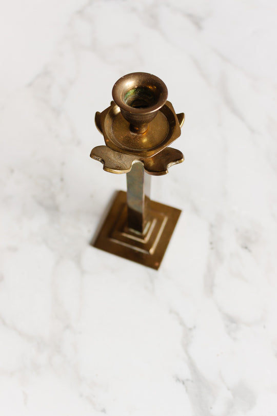 A pair of brass candleholders with square bases and decorative detailing, displayed on a white marble surface; their dimensions enhance an elegant and timeless appeal.