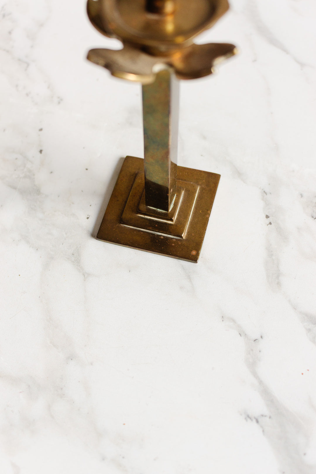 A pair of candleholders with square brass bases are set on a white marble surface with gray veining. The photo, focused on the lower section, showcases the elegant proportions and dimensions of each piece.