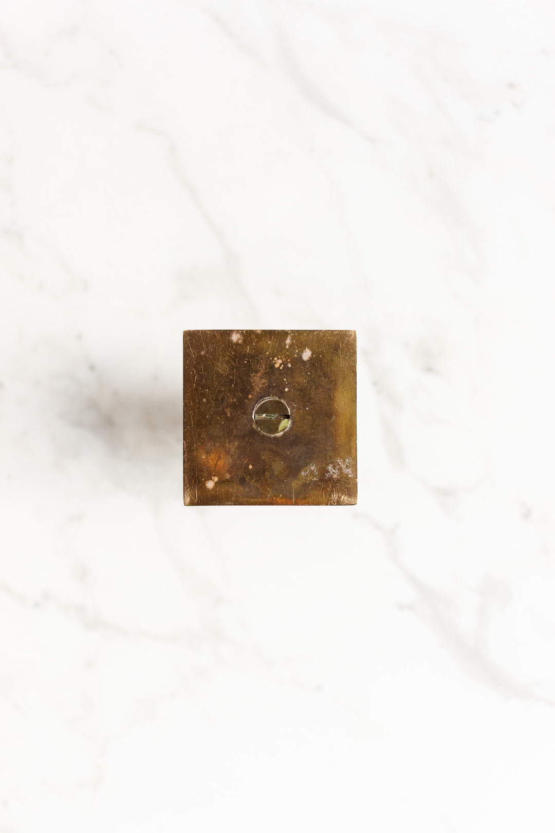 A pair of square brass candleholders with precise dimensions and a central circular indentation, viewed from above on a white marble surface.