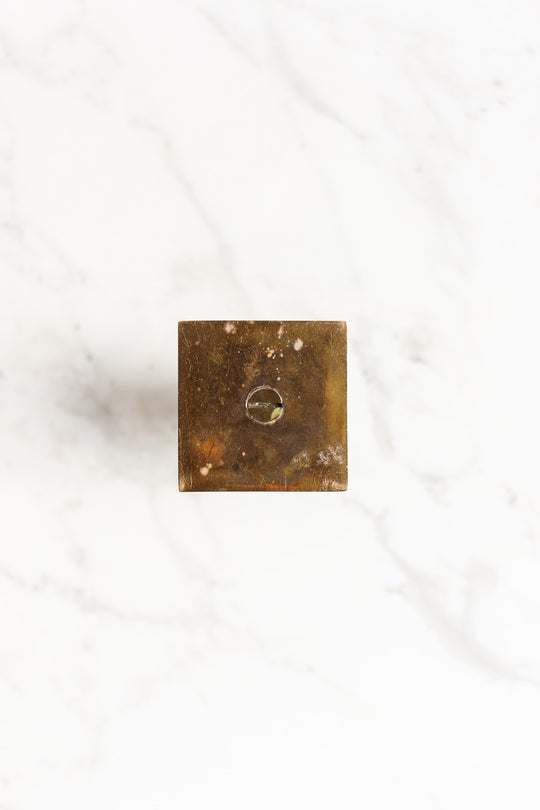 A pair of square brass candleholders with precise dimensions and a central circular indentation, viewed from above on a white marble surface.