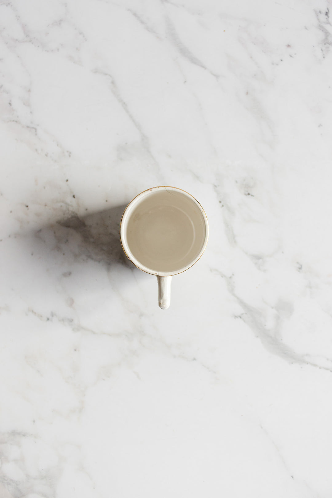 An antique Gien transferware coffee cup filled with clear water rests on a white marble surface, viewed from above, showcasing the elegant design and details of the cup and its refined surroundings.