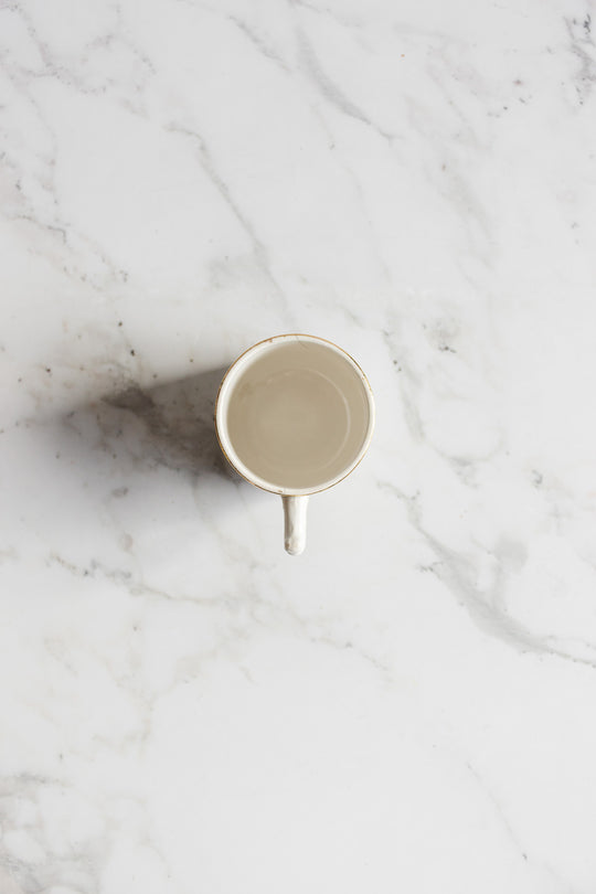 An antique Gien transferware coffee cup filled with clear water rests on a white marble surface, viewed from above, showcasing the elegant design and details of the cup and its refined surroundings.