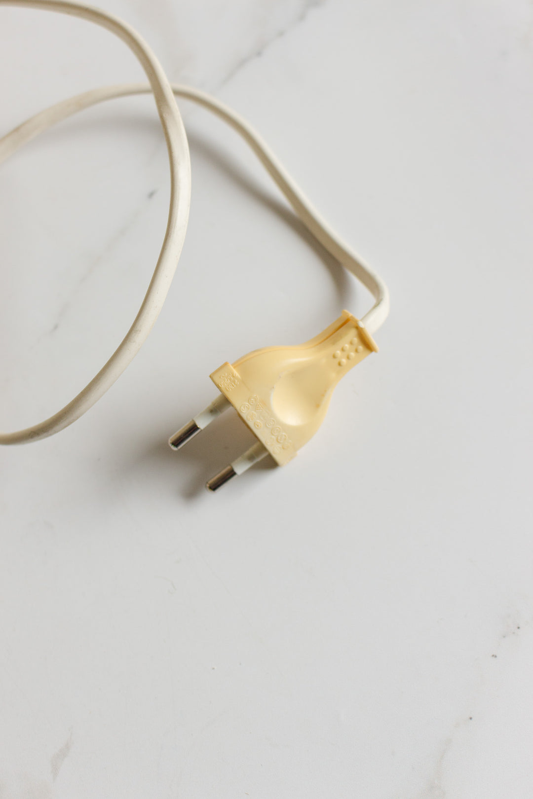A vintage French alabaster table lamp with a white electrical cable and a yellowed, two-pronged plug rests on a white surface.