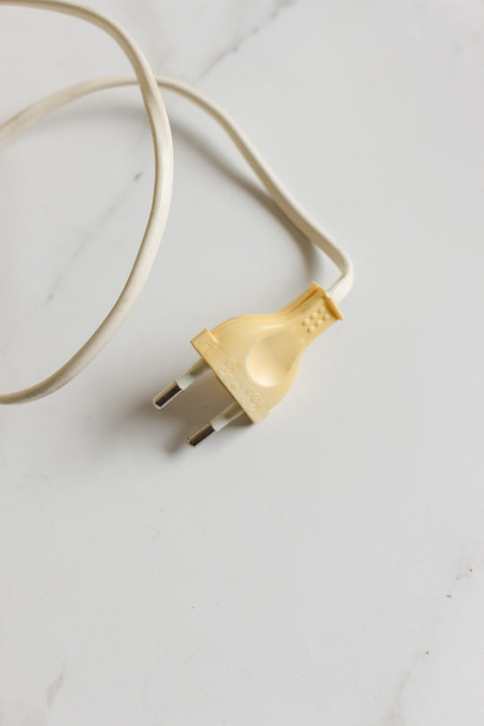 A vintage French alabaster table lamp with a white electrical cable and a yellowed, two-pronged plug rests on a white surface.